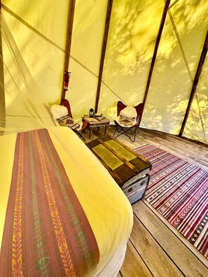 Ein Zelt mit Bett, Stühlen, einem kleinen Tisch und einem Teppich.
