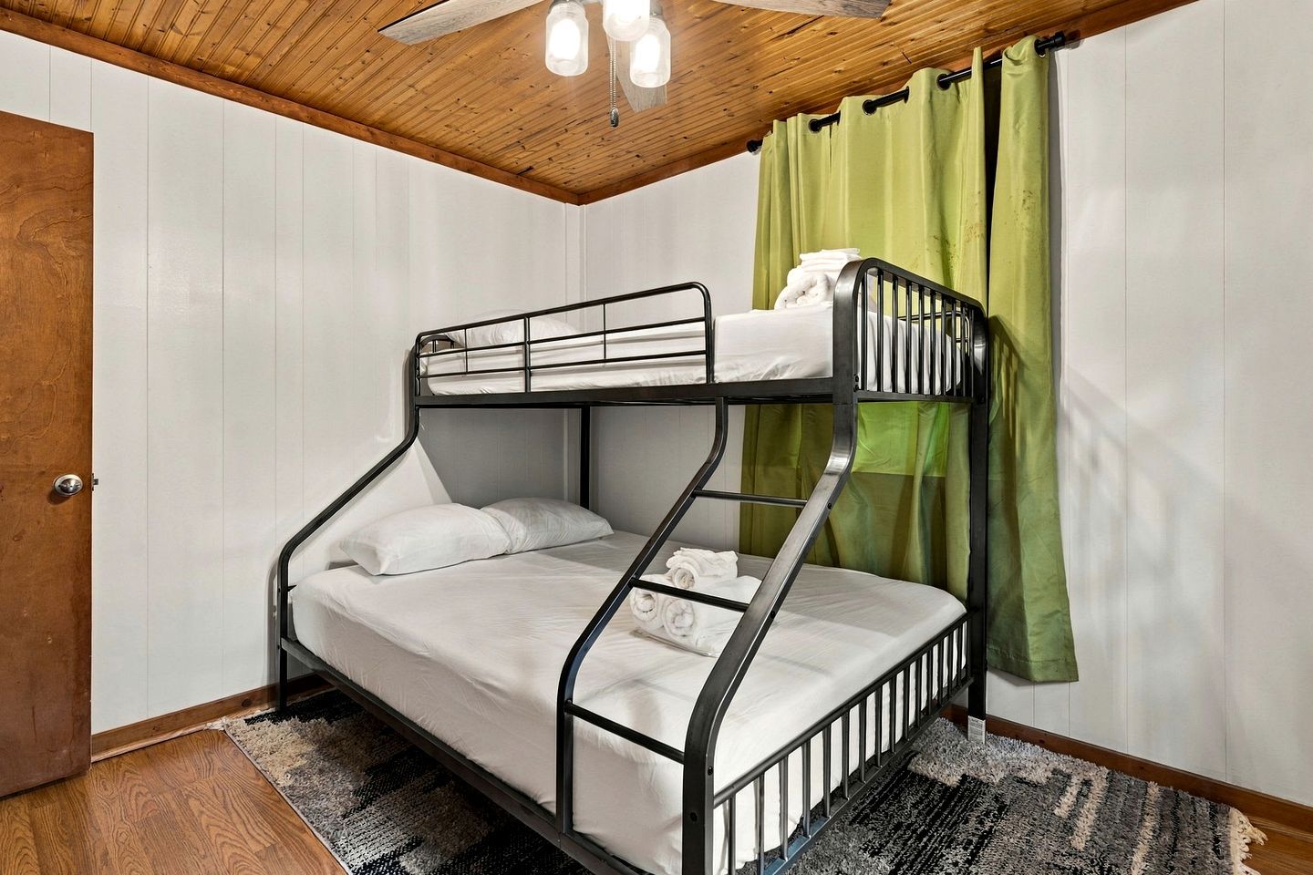 Un lit superposé avec un plafond en bois et un rideau vert.