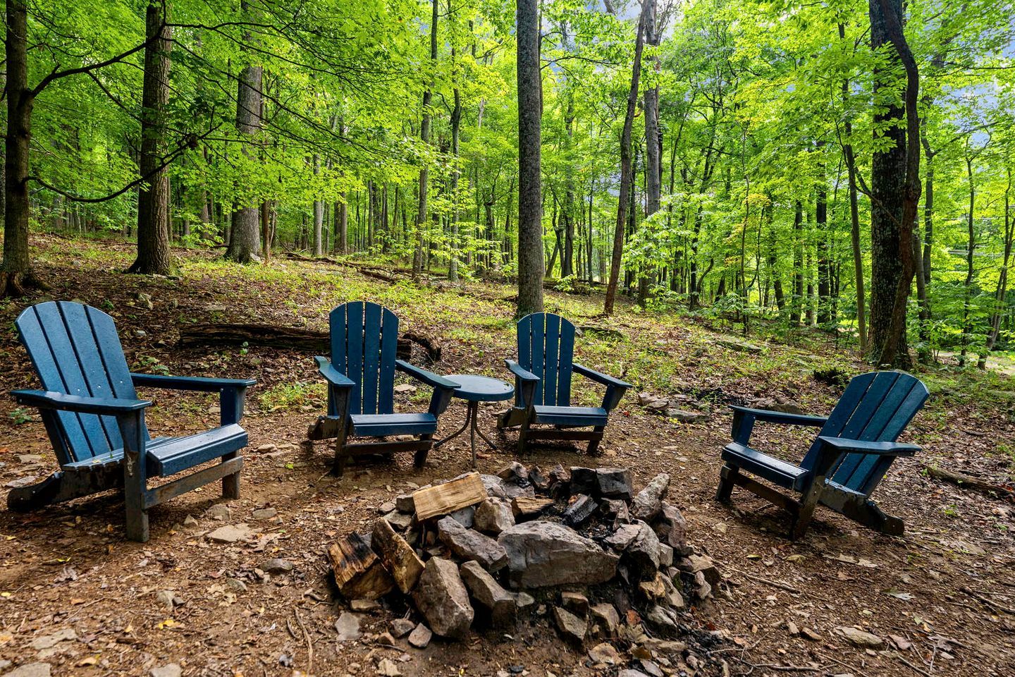 Un décor forestier avec quatre chaises Adirondack disposées autour d’un feu de camp.