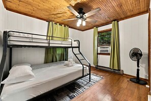 Habitación con literas, ventilador de techo, ventilador de pie y ventana con cortinas.