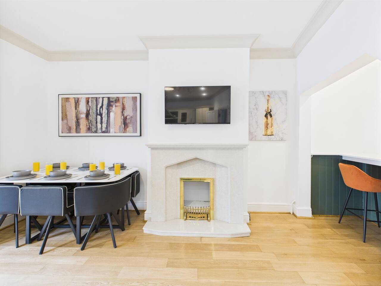 Un comedor con chimenea blanca, un televisor montado encima y obras de arte en las paredes.