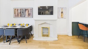 Ein Essbereich mit einem weißen Kamin, einem darüber montierten Fernseher und Kunstwerken an den Wänden.