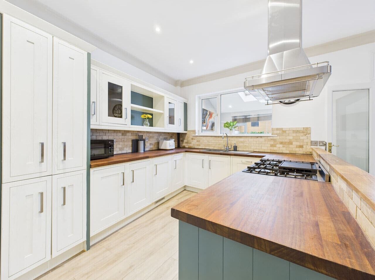 A modern kitchen with white cabinets, a wooden countertop, and a stainless steel range hood.