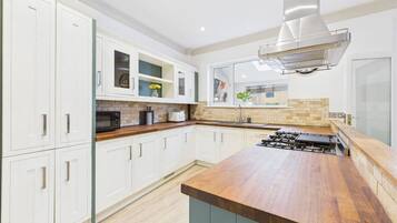 A modern kitchen with white cabinets, a wooden countertop, and a stainless steel range hood.