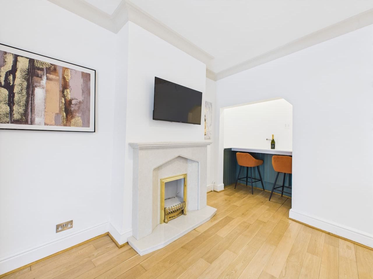 Una sala moderna con chimenea, televisor montado y comedor con taburetes de bar.