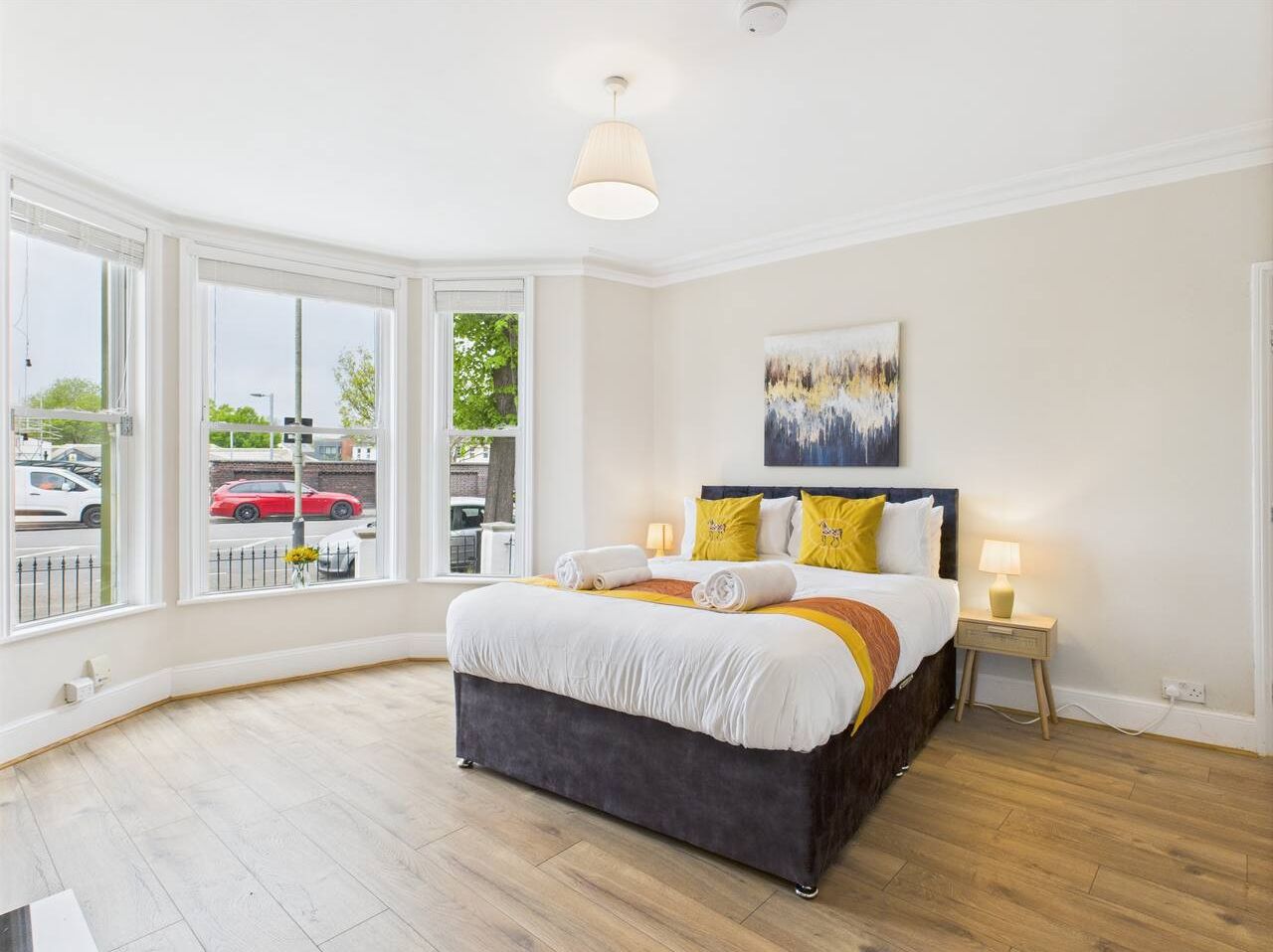 Un dormitorio amplio con una cama grande, vista por la ventana y un cuadro en la pared.