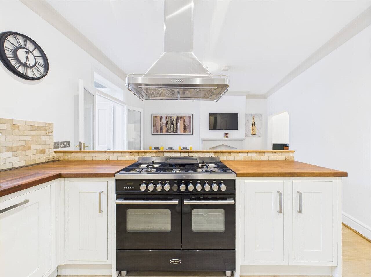 A kitchen with a stainless steel stove, white cabinetry, and a brick backsplash.