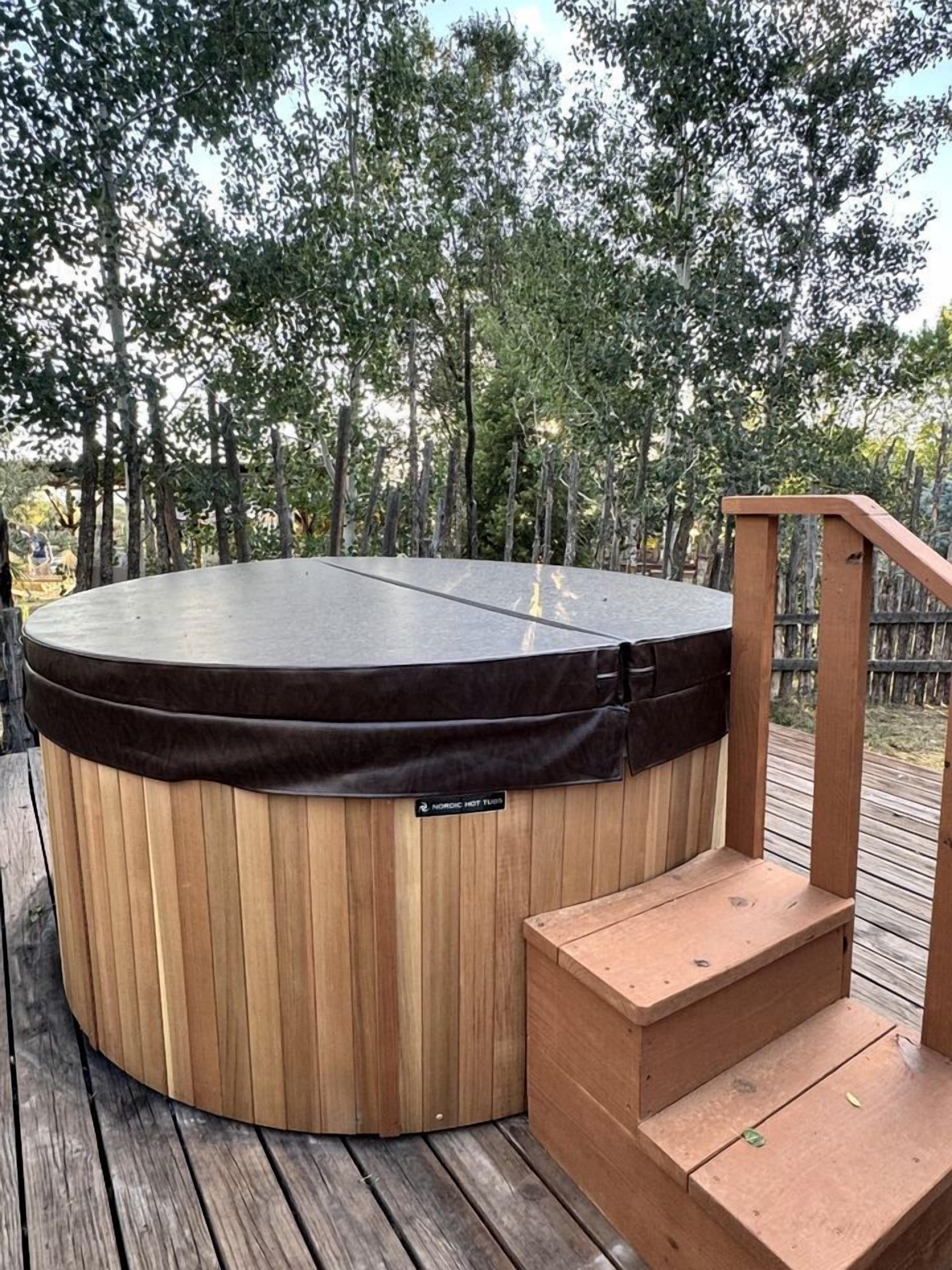 A hot tub on a wooden deck with a wooden staircase leading up to it.