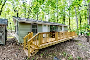 A cabin with a wooden deck and a small porch, surrounded by trees. - Charming Dog-Friendly Cabin with Hot Tub and Fire Pit - Pond Access Makes This the Perfect Cabin for Your Fishing Getaway in Berkeley Springs, WV (Berkeley Springs)