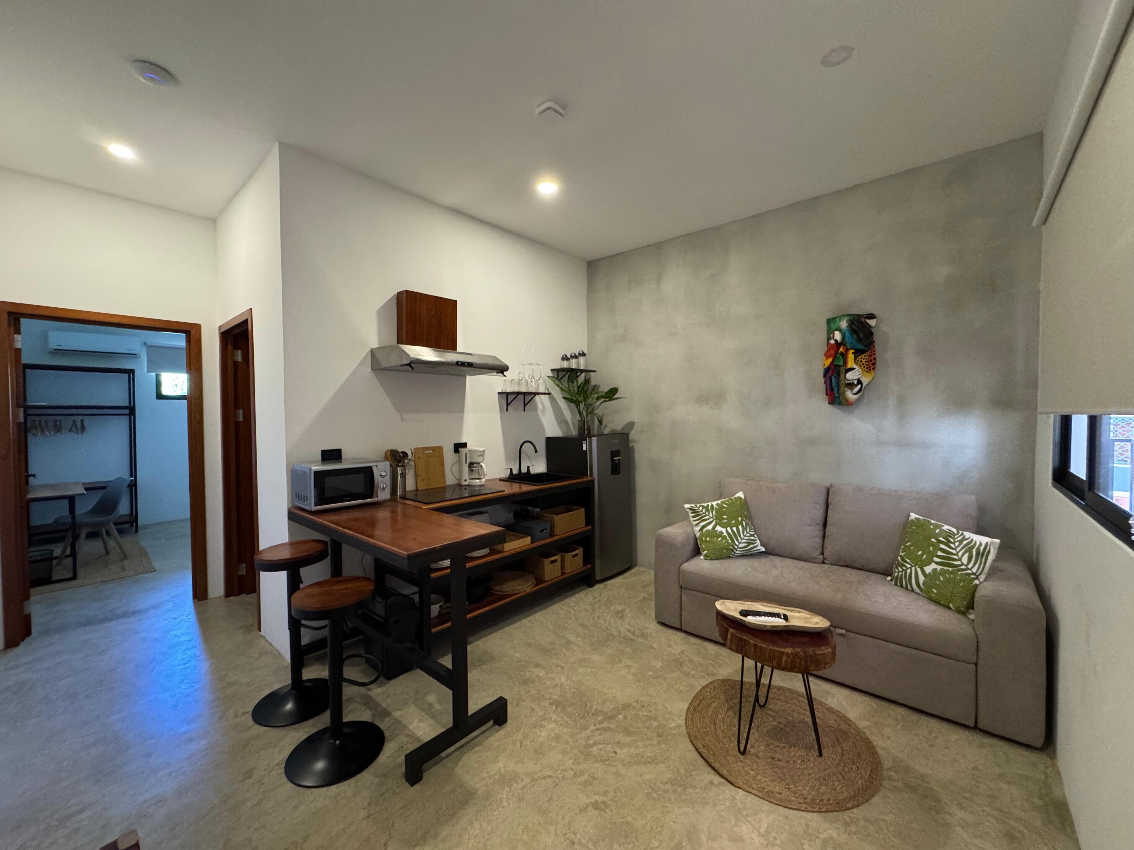 Una sala moderna con sofá, mesa de centro y comedor, con una cocina al fondo.
