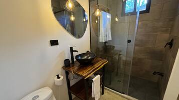 Ein modernes Badezimmer mit rundem Spiegel, Waschbecken in Schwarz, Toilette und Duschkabine aus Glas.