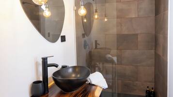 Un baño moderno con un espejo redondo, tocador de madera y ducha con cerramiento de vidrio.