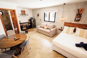 Una habitación de hotel compacta con cama, sofá, mesa de comedor y kitchenette.