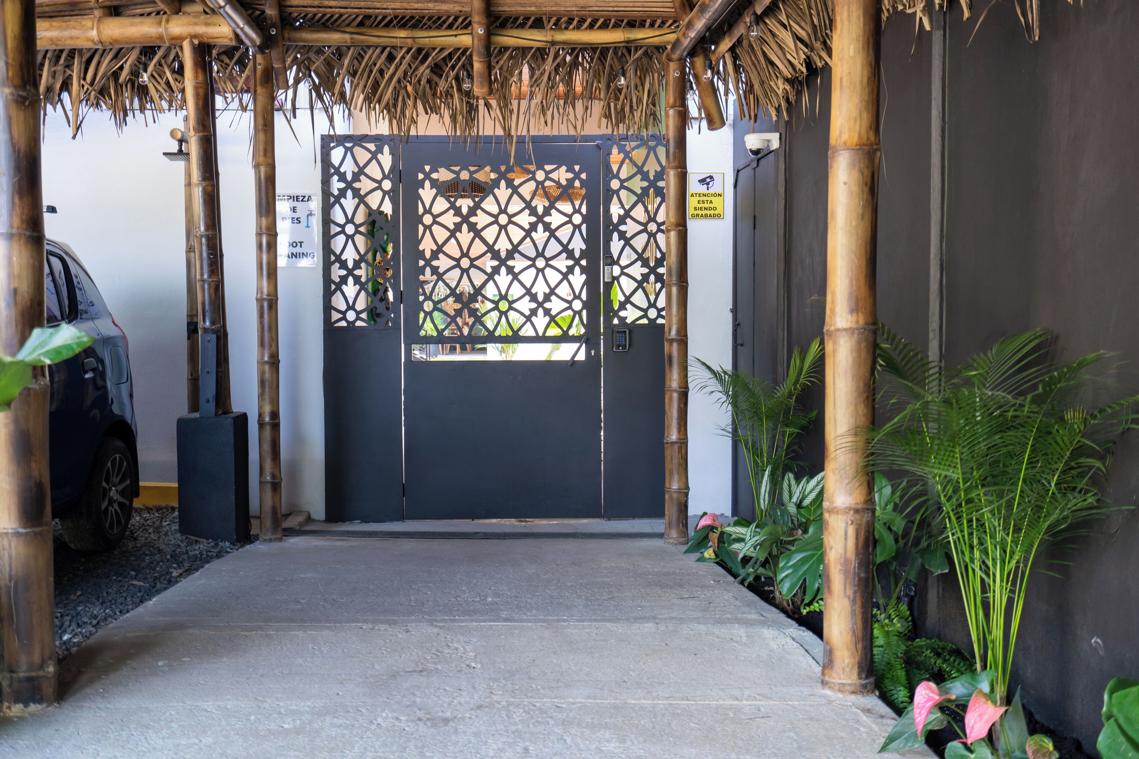 A covered entrance with a dark door, bamboo pillars, and a car parked to the left.