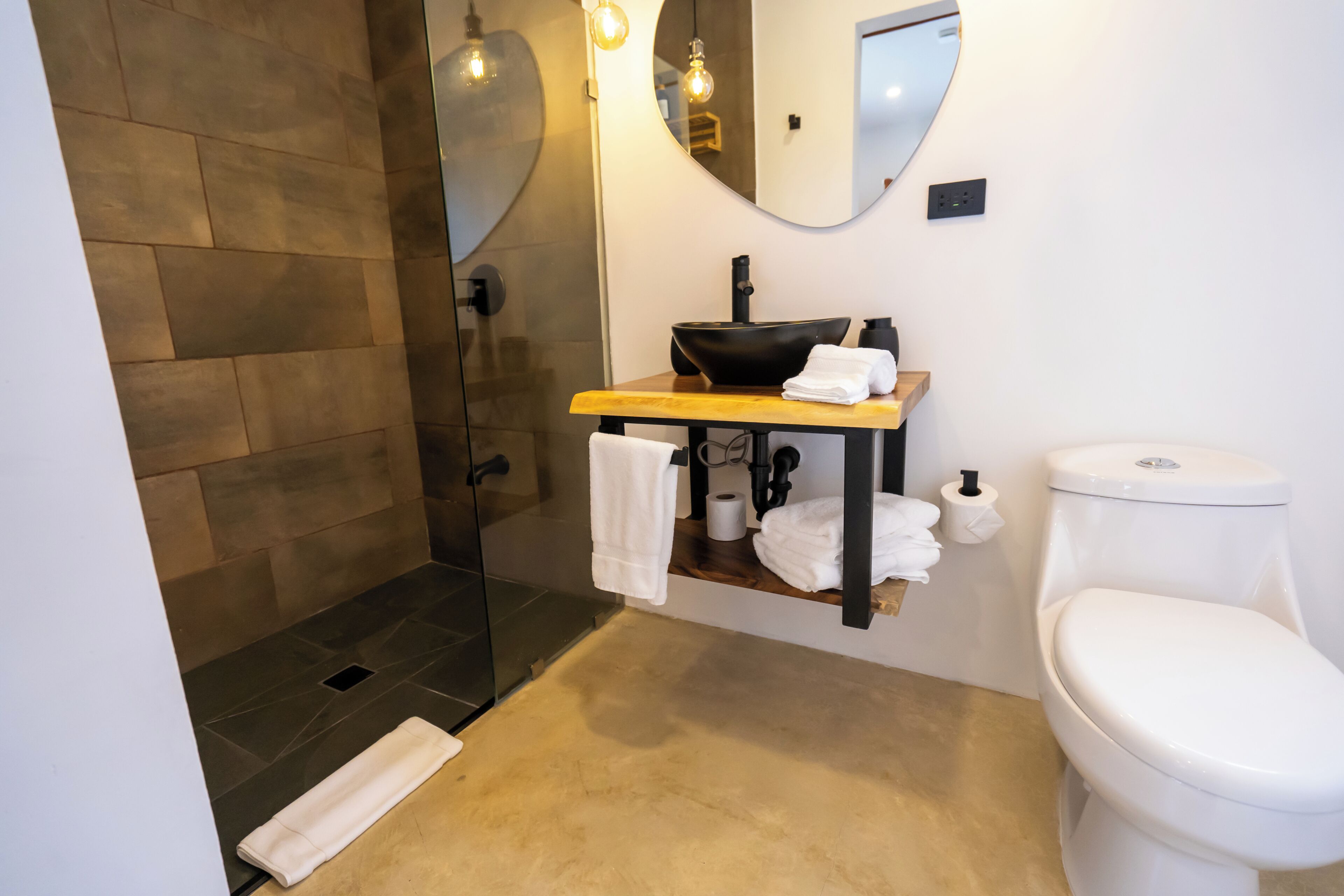 Un bagno con doccia vetrata, un mobile bagno in legno, un water bianco e uno specchio.