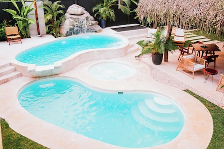 A swimming pool with a waterfall feature, surrounded by lounge chairs and a small waterfall.