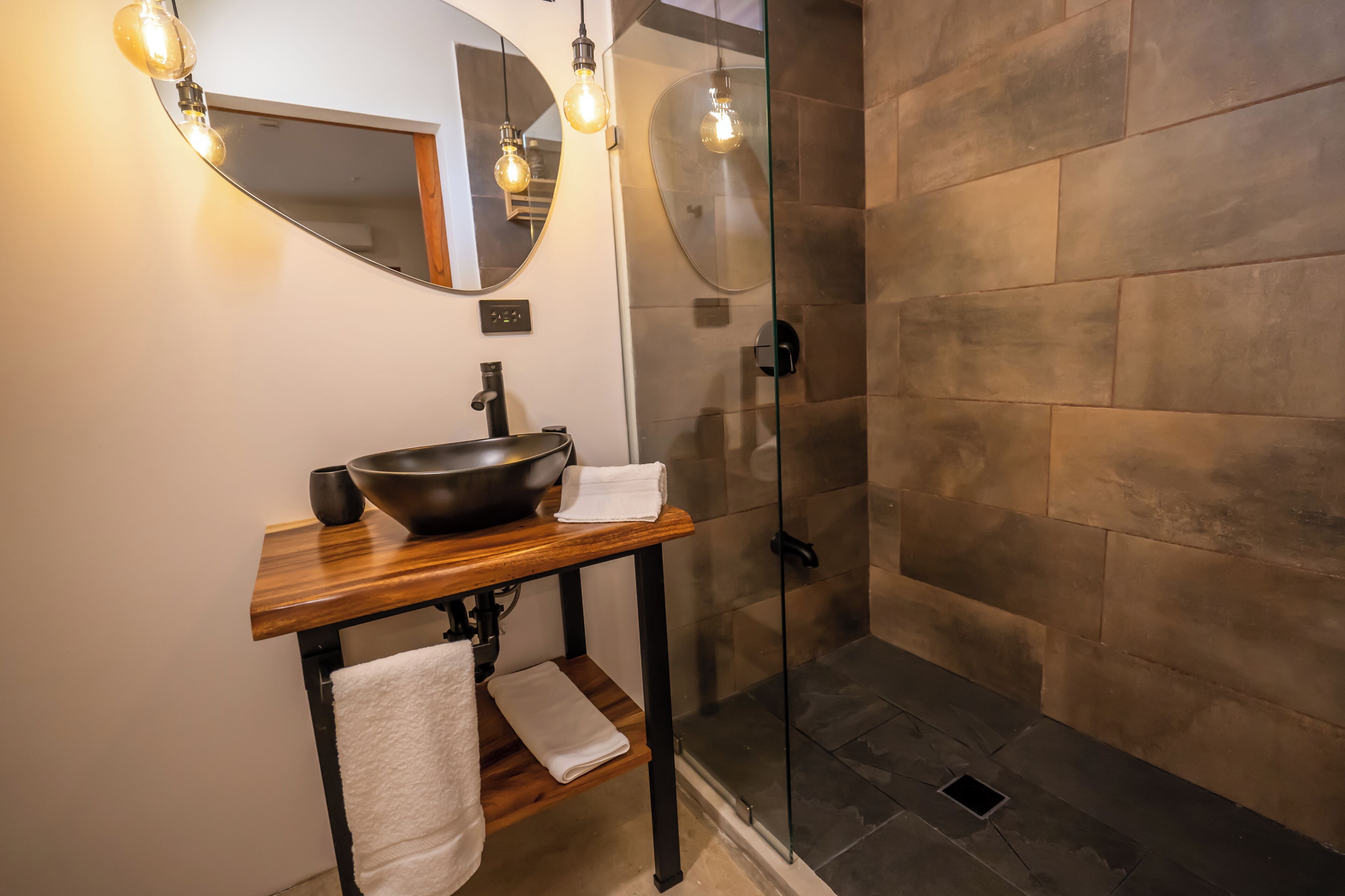 Un bagno con un mobile contenitore in legno, un lavabo capiente, uno specchio e un box doccia in vetro.