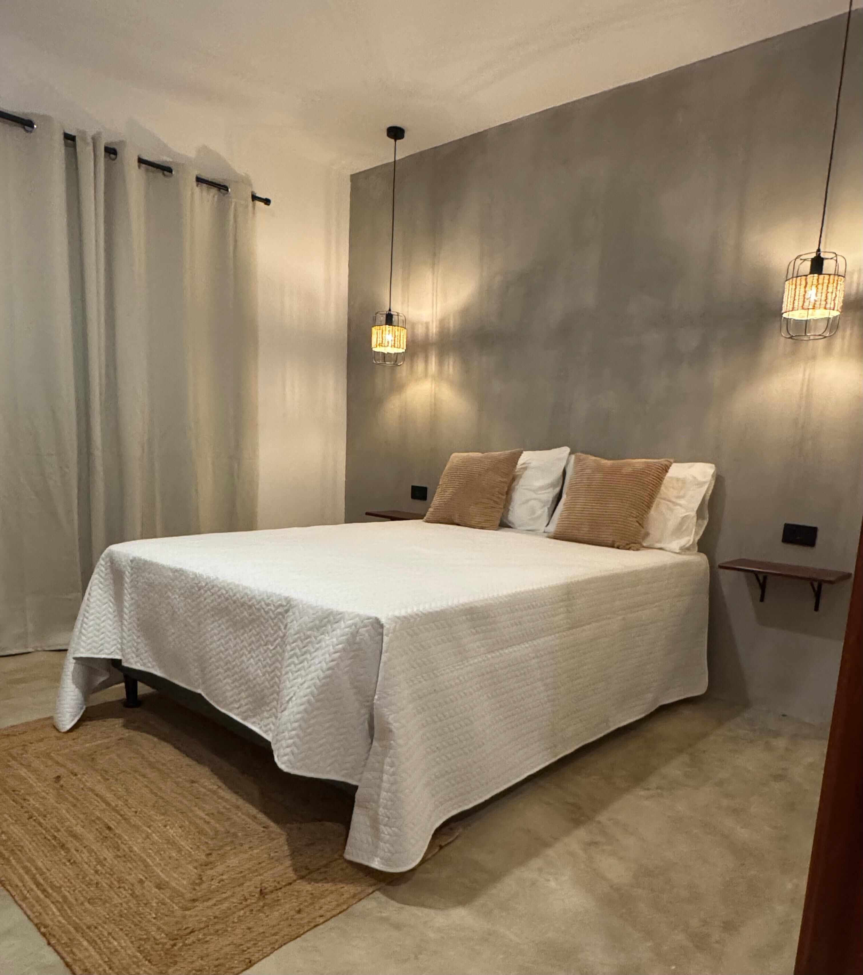 A bedroom with a large bed, two bedside tables, a rug, and two pendant lights.
