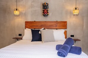 A neatly made bed with rolled towels, two bedside tables, a wooden headboard, and two wall-mounted lamps. - Bahia Selvatica Lodge (Uvita)