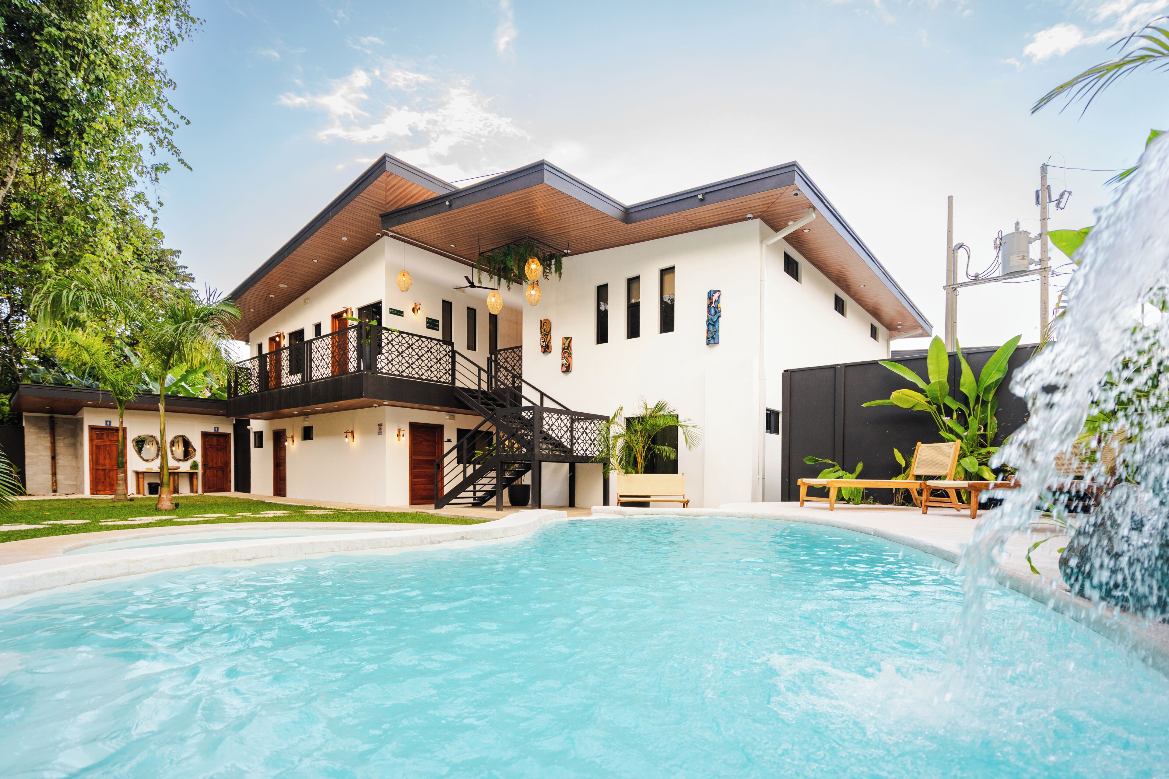A modern building with a swimming pool, a waterfall feature, and a balcony with outdoor seating.