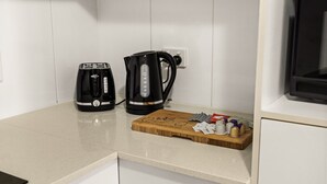 Una cocina equipada con cafetera, tostadora y tabla de cortar con utensilios.
