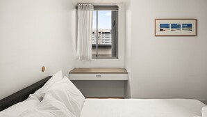 Una habitación de hotel con cama, escritorio con cajón, ventana con cortinas y un cuadro en la pared.