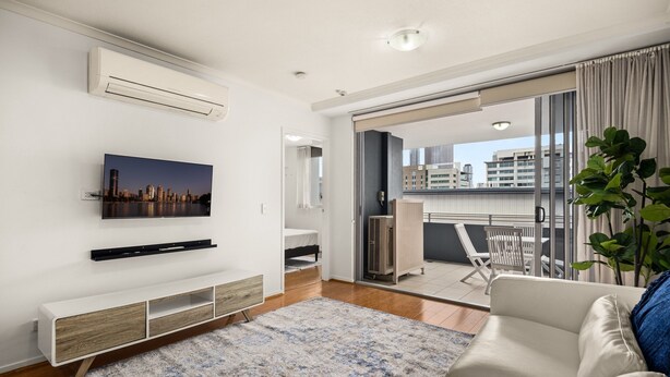 Una sala de estar moderna con un televisor de pantalla plana, un sofá blanco y un ventanal con vistas a la ciudad.