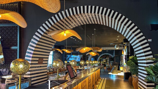Un intérieur d’hôtel luxueux, caractérisé par des arches à rayures noires et blanches originales, un bar bien éclairé et une esthétique moderne.