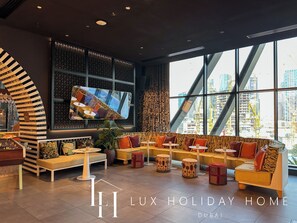 A modern lounge area with a sofa set, round tables, and a large TV screen. - LUX | The Five Star Modern Suite (Dubai)