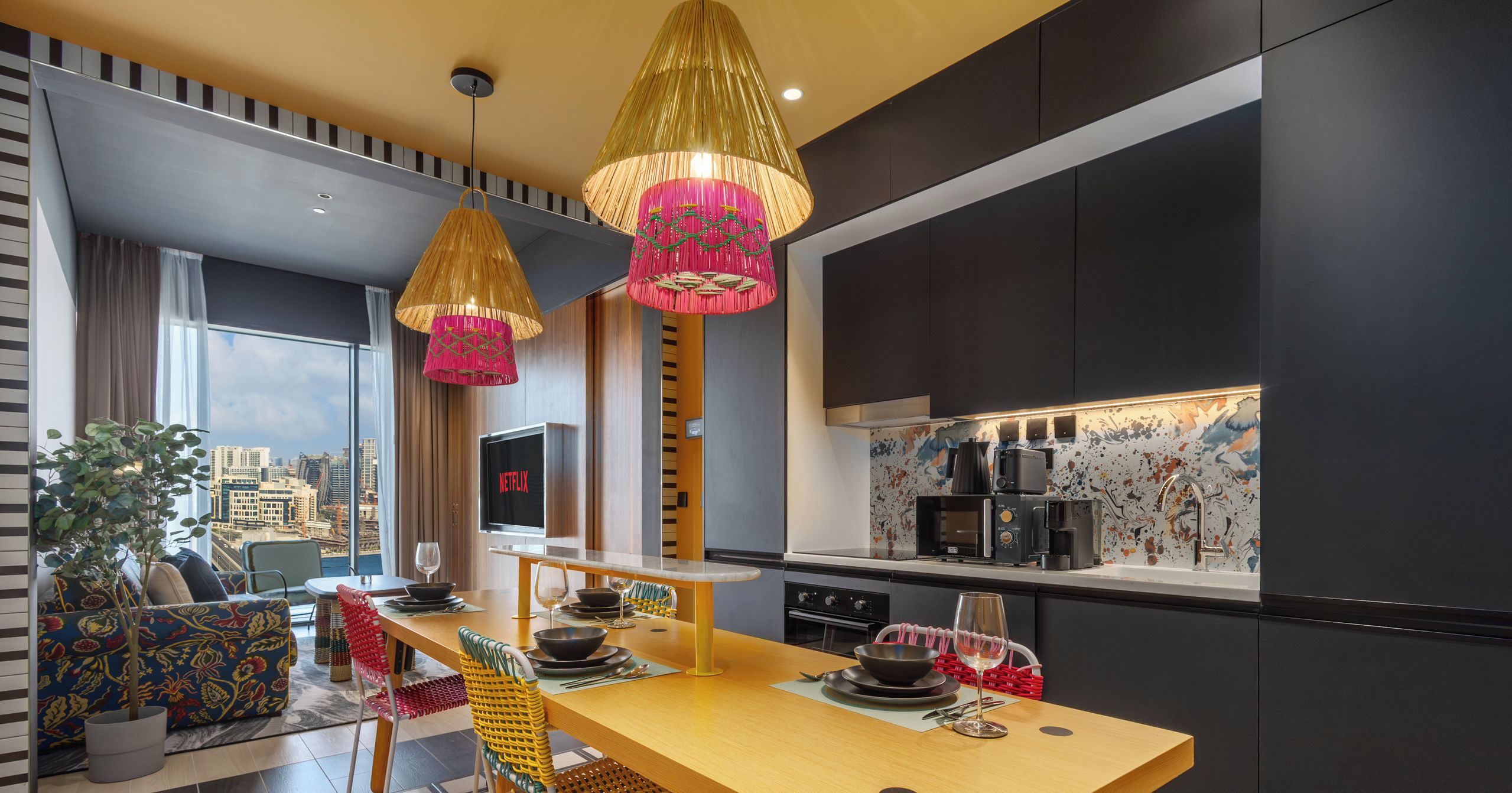 Une cuisine moderne avec vue sur la ville, un coin repas avec une table et des chaises en bois, et un salon avec un canapé et une plante.