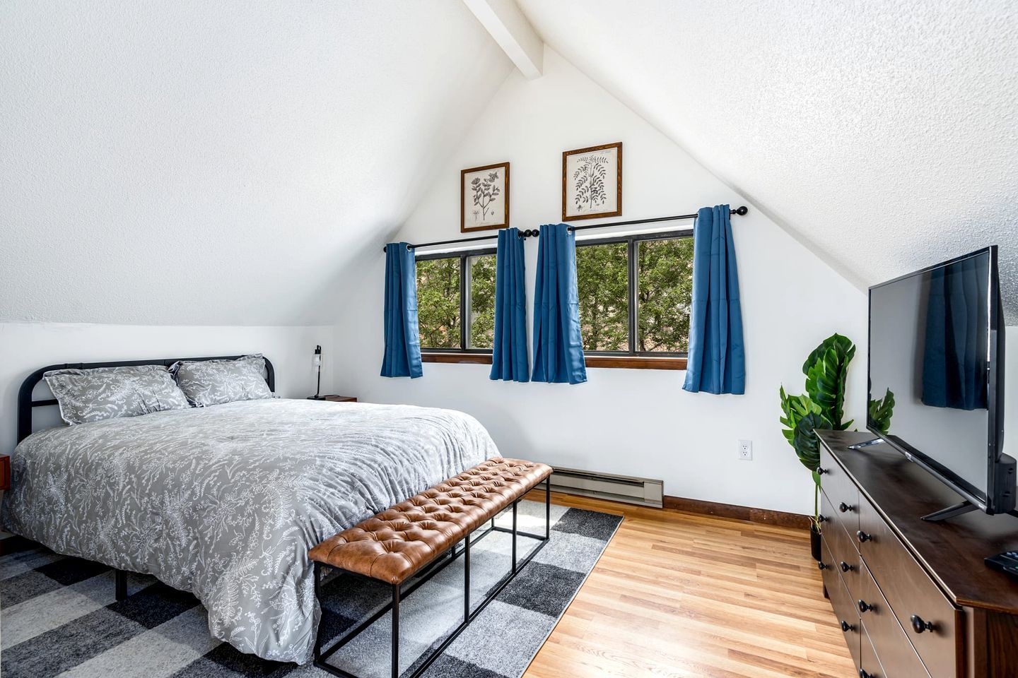 A bedroom with a bed, bench, TV, and windows with curtains.