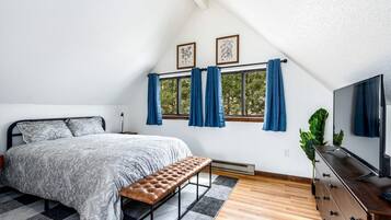 A bedroom with a bed, bench, TV, and windows with curtains.