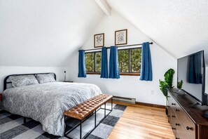 A bedroom with a bed, bench, TV, and windows with curtains.