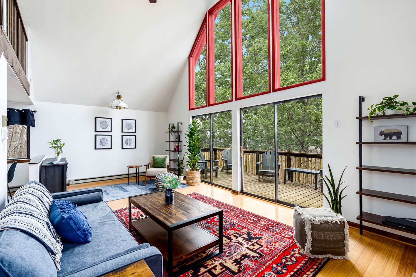 A spacious living room with a large window, a wooden coffee table, a sofa, and a red rug.