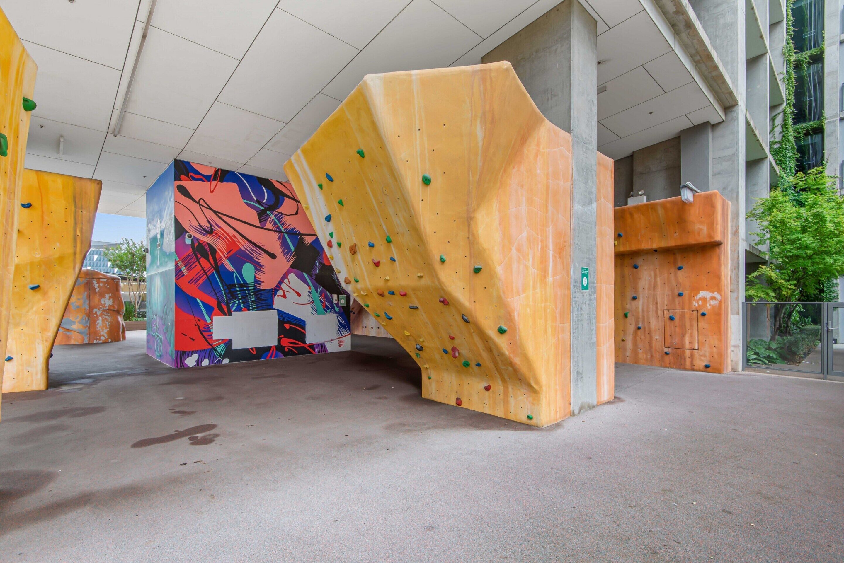 Un mur d’escalade intérieur, doté de prises colorées et orné d’une fresque murale éclatante en arrière-plan.