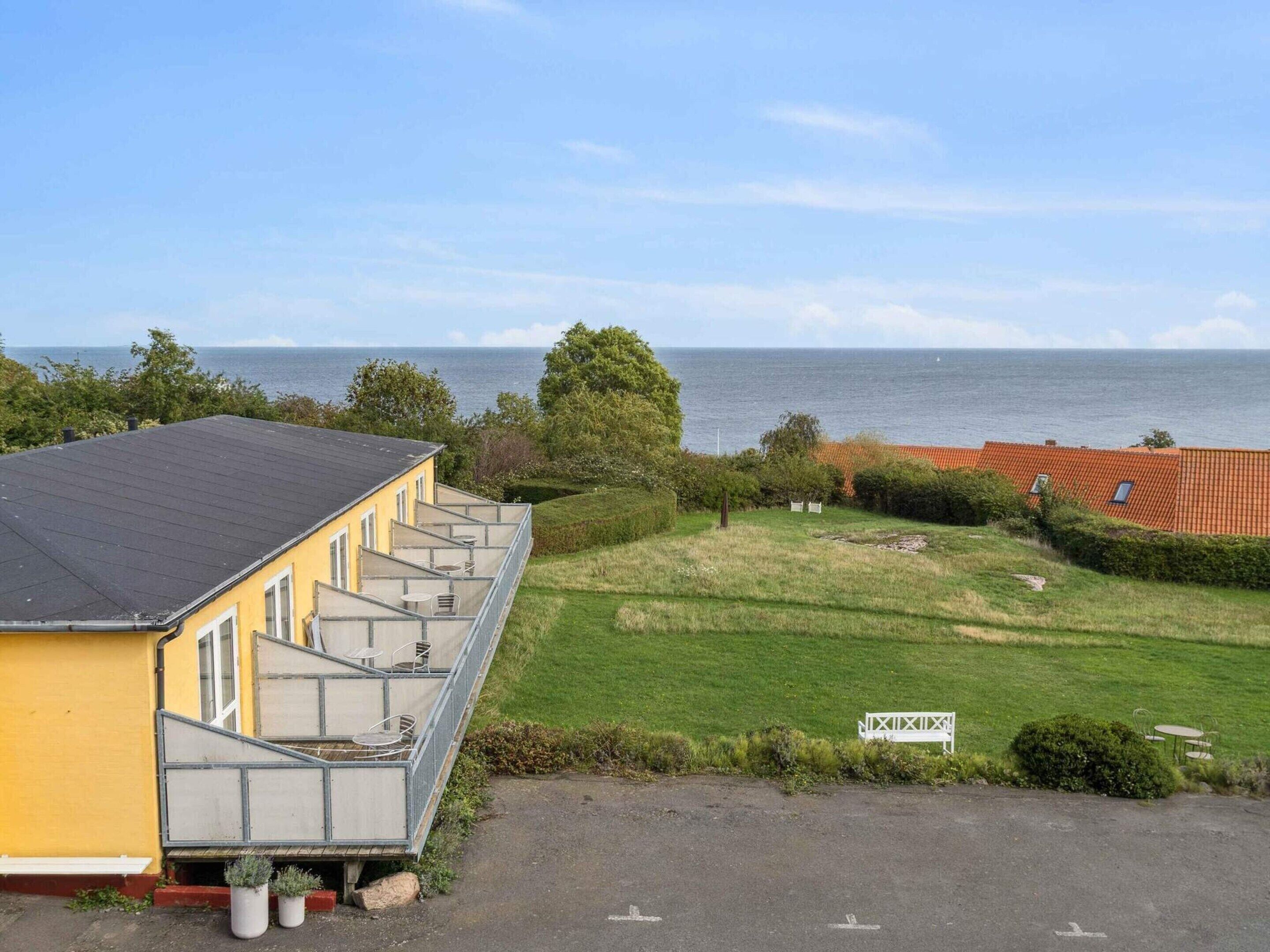 A yellow building with a balcony overlooking a grassy area and the sea.