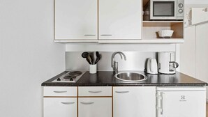 Una cucina compatta con mobili bianchi, un forno a microonde, una macchina da caffè e un lavello.