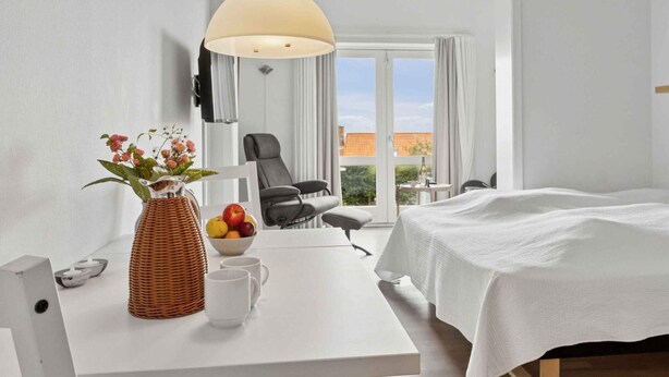 Camera d'albergo con un letto, una scrivania con un vaso di fiori, una ciotola di frutta e vista sull'esterno.