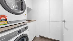A compact laundry room with a front-loading washing machine and a dryer stacked on top. - Stylish Brisbane City Stay With Bbq, Pool & Gym (Brisbane)