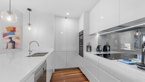 A modern kitchen with white cabinetry, a wooden floor, a built-in dishwasher, and a stainless steel range hood. - Stylish Brisbane City Stay With Bbq, Pool & Gym (Brisbane)