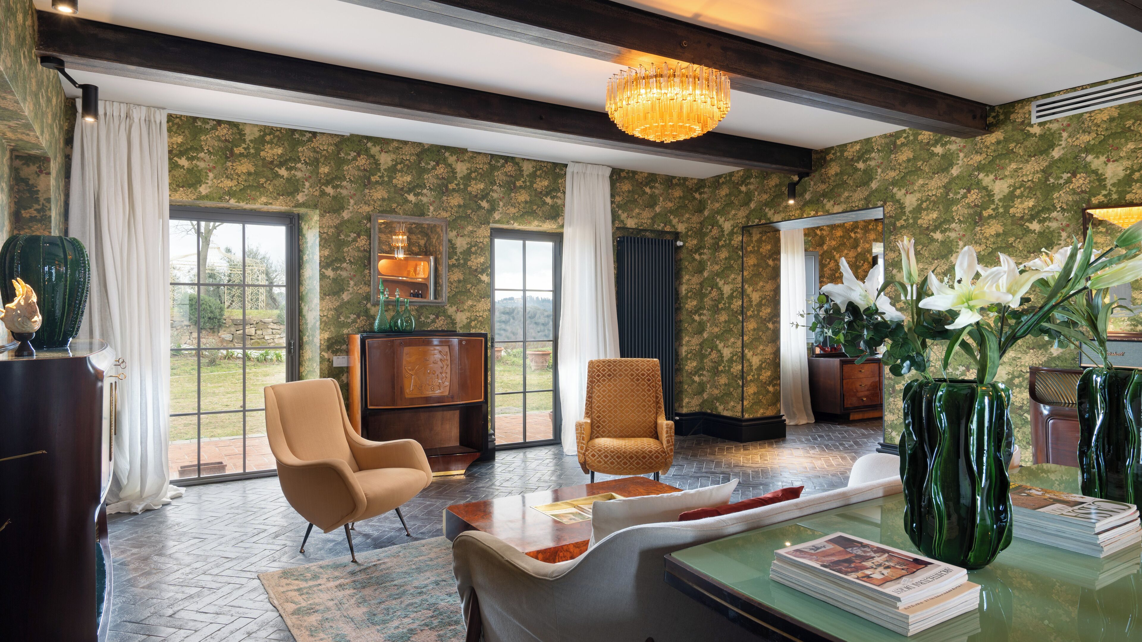 A spacious room with a large window, a chandelier, and a wooden coffee table with magazines.