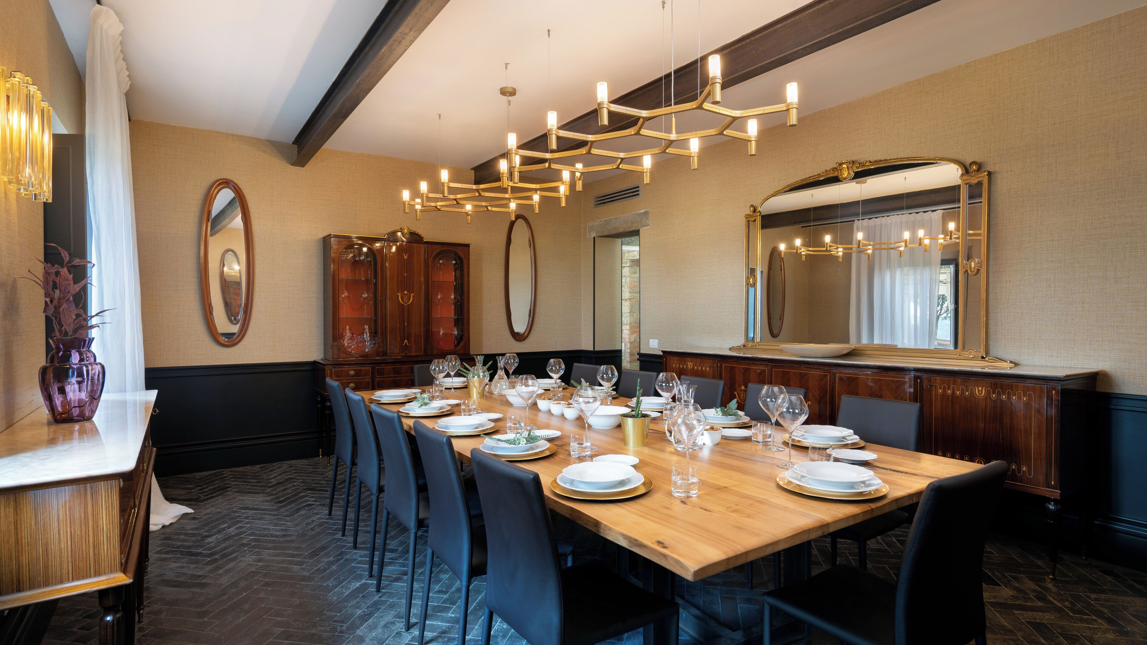 A dining room with a long wooden table set for a meal, surrounded by chairs.