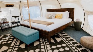 A tented accommodation with a single bed, a bench, a small table, and a waste bin. - Lovely Bell Tent Rentals for Intimate Escapes in Spicewood, Texas (Spicewood)