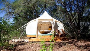 A dome-shaped tent with a bed inside, surrounded by trees. - Lovely Bell Tent Rentals for Intimate Escapes in Spicewood, Texas (Spicewood)