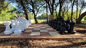 A large outdoor chessboard with pieces arranged for a game, surrounded by trees and a clear sky. - Glamping Retreat in Texas in this Wonderful Bell Tent Rental in Spicewood (Spicewood)