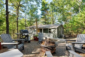 A cabin with a deck, surrounded by trees, with Adirondack chairs and a grill. - Cozy Modern Cabin with Fire Pit & Trail Access near Berkeley Springs, West Virginia (Hedgesville)