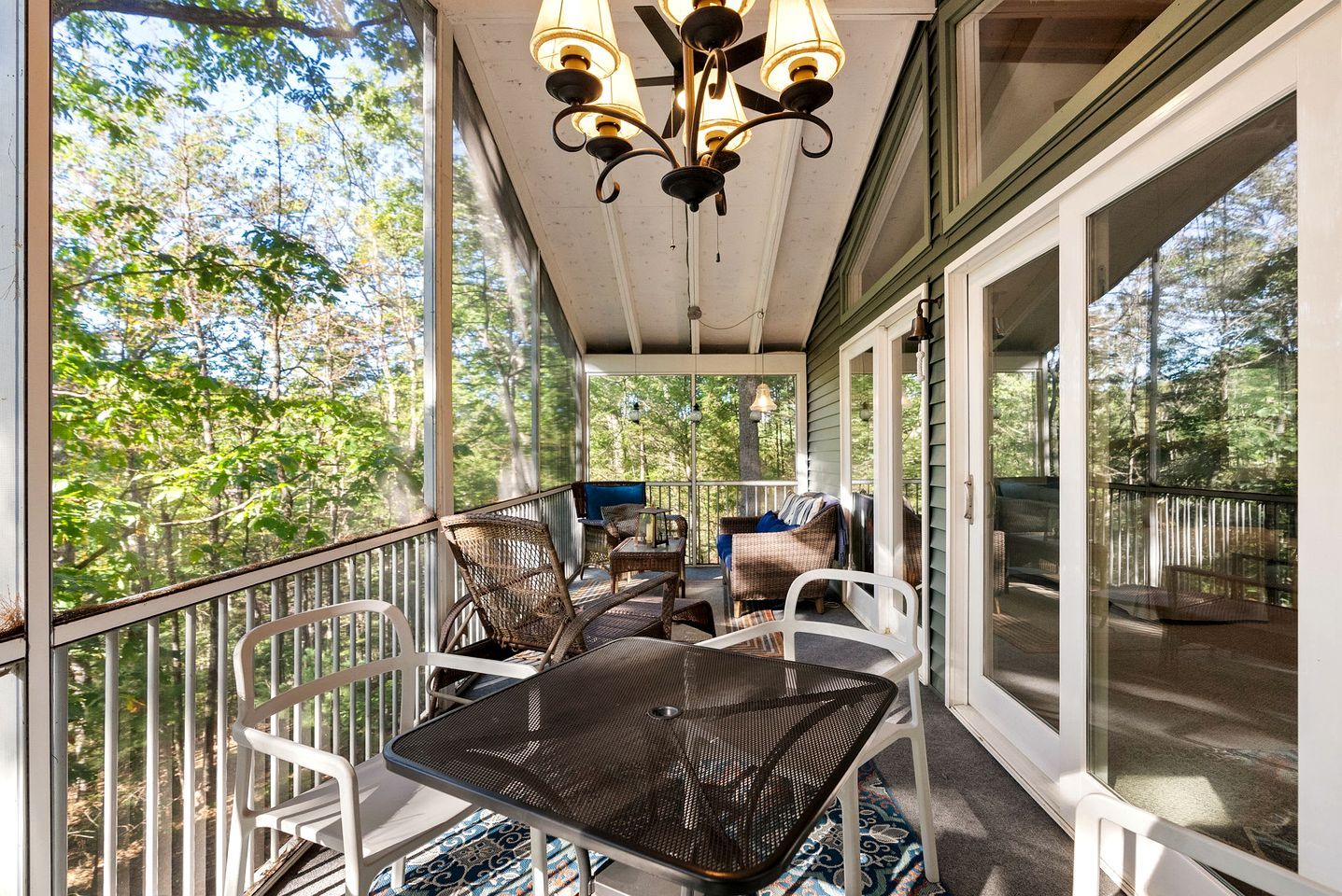 Varanda coberta com móveis de exterior, uma mesa e cadeiras, com vista para uma área arborizada.