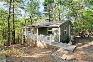 A small cabin with a porch, surrounded by trees.