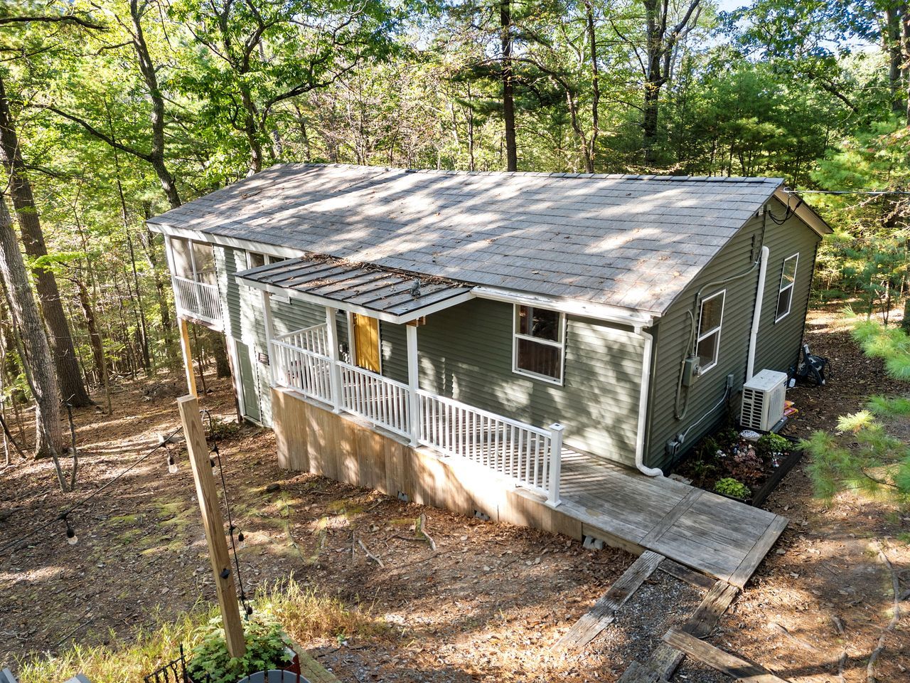Une petite cabane à un seul étage, dotée d’un porche et d’une rampe d’accès, et entourée d’arbres.