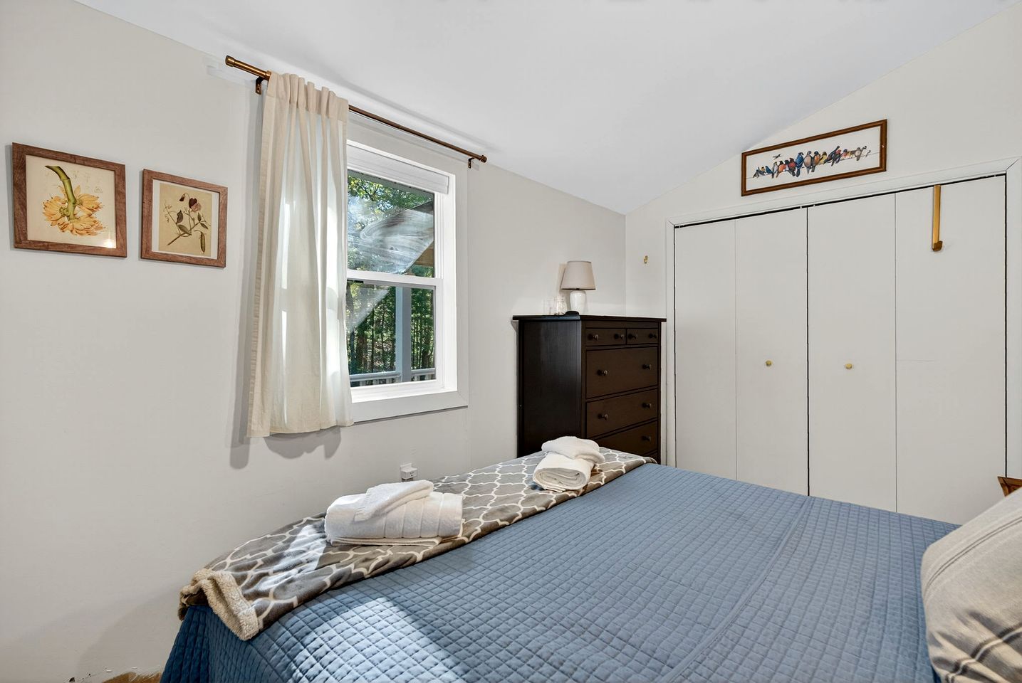 Ein Schlafzimmer mit einem Bett, einem Schminktisch, einem Fenster mit Vorhängen und einer Wandlampe.